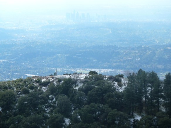 Zoom in view looking down on a lightly snow covered Echo Mountain with Downtown Los Angeles in the background from the Castle Canyon Trail.