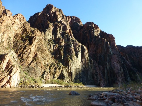View of the Colorado River with large rock sticking out of it and similar shaped point atop the canyon wall beyond.